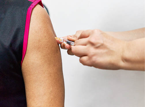 Hand of nurse holding hypodermic syringe is injecting vaccine of flu with left shoulder of man in black sleeveless sports shirt  Close up shoulder of man  Healthcare and medical concept photography 