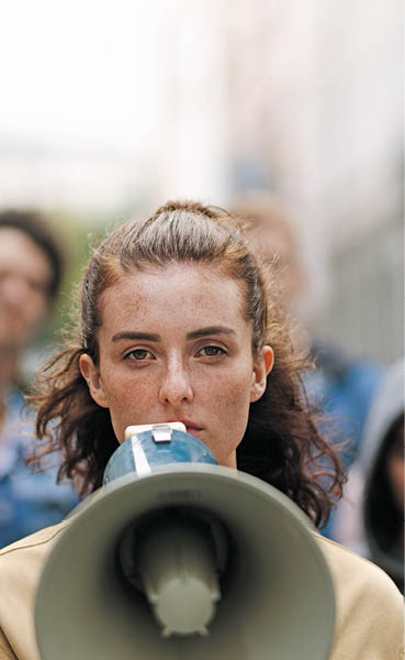 Young woman with a megaphone with group of demonstrator in background  Woman protesting with megaphone in the city 