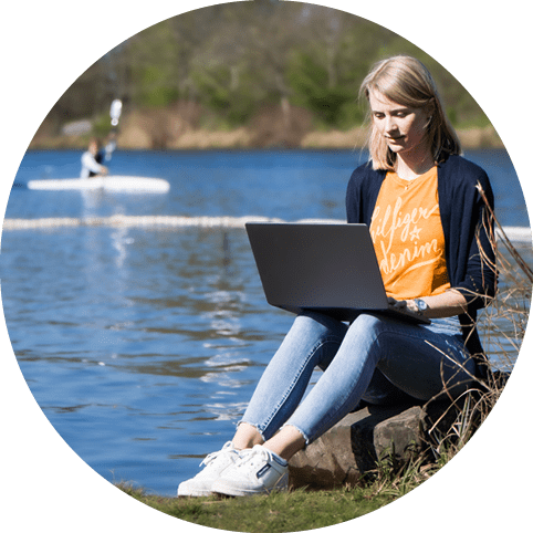 Sportlerin sitzt an einem See und schreibt auf einem Notebook eine Geschichte
