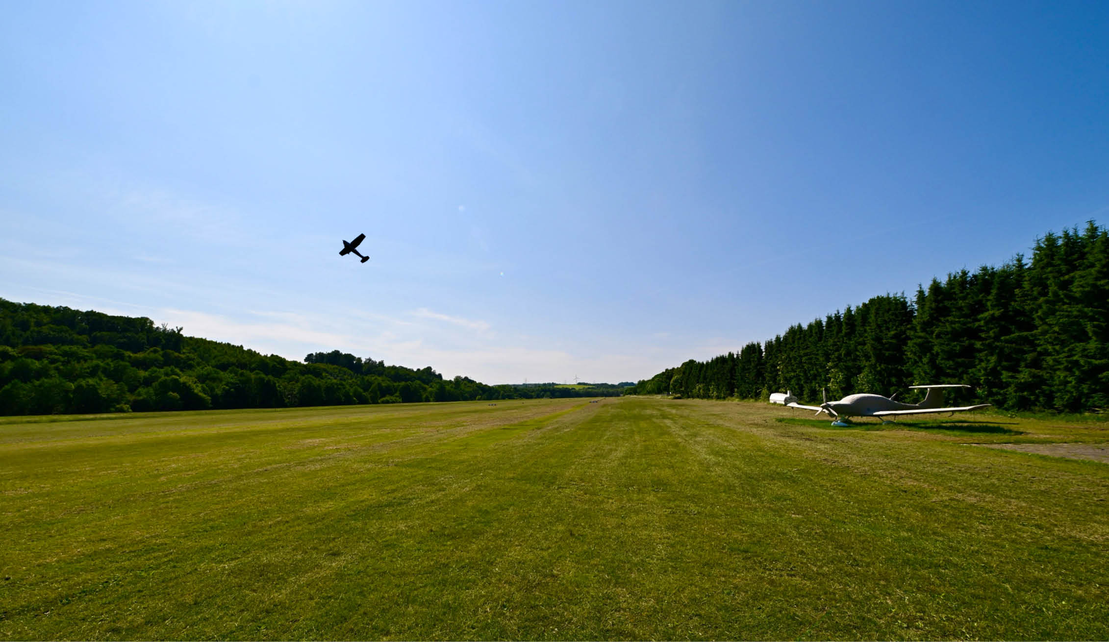Flugfeld, Flugplatz eines Sportflugvereins. Im Hintergrund startet ein Flufzeug ber der gr nen Wiese. 