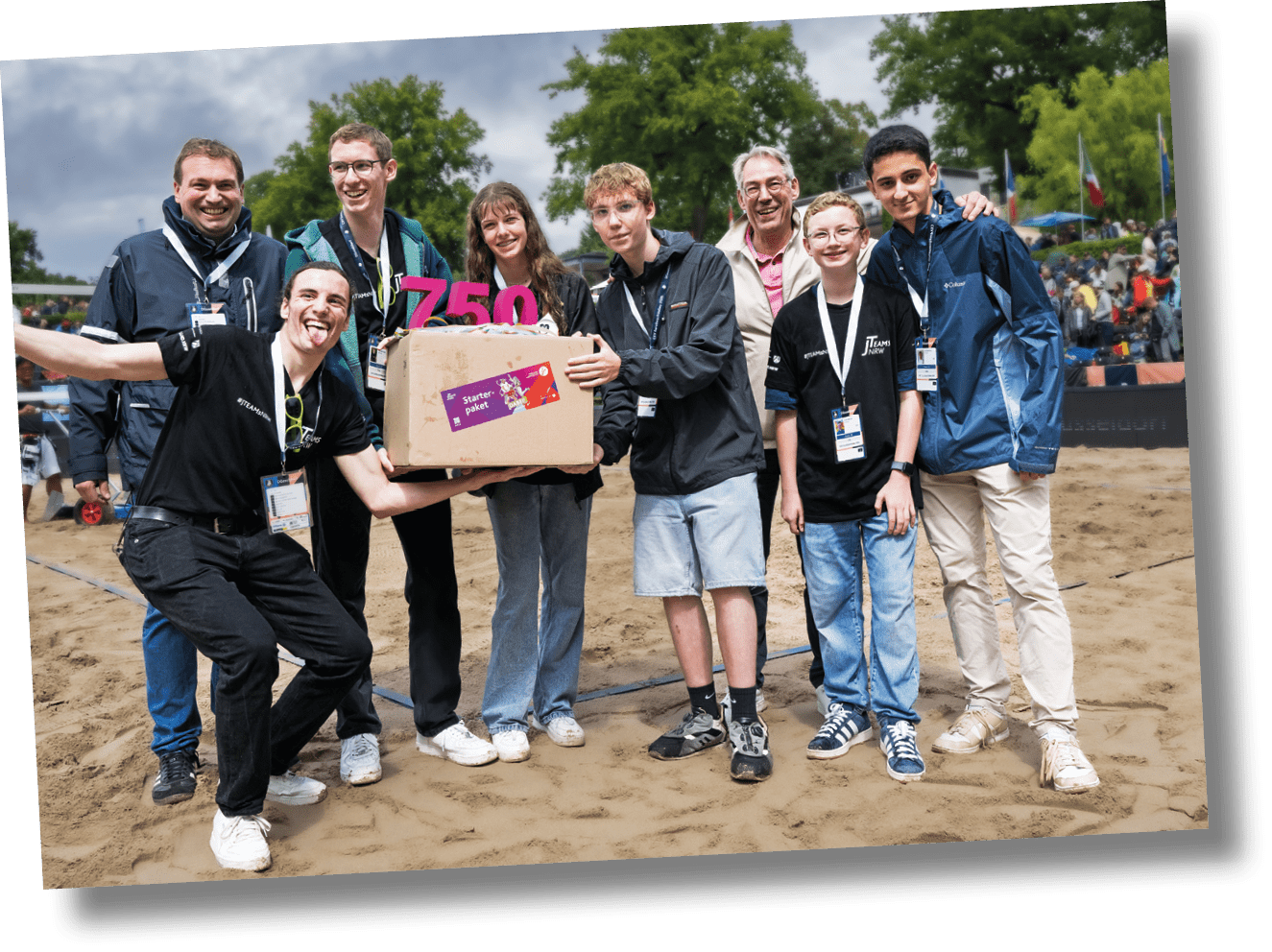 Mehrere Personen stehen mit einer Schrift 750 J-Teams und einem Karton auf einer Wiese
