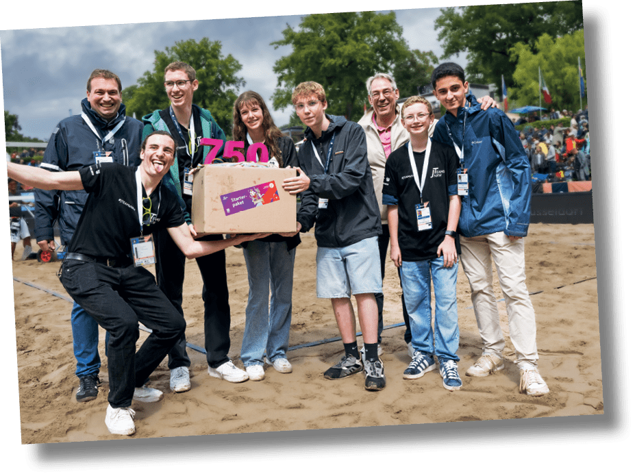 Mehrere Personen stehen mit einer Schrift 750 J-Teams und einem Karton auf einer Wiese