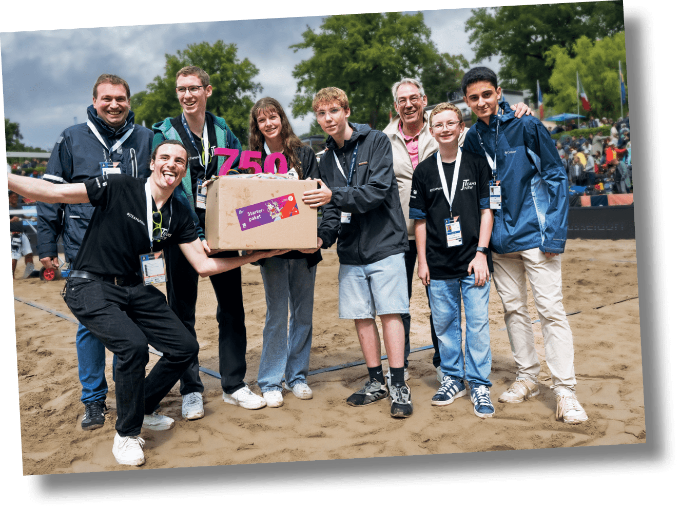 Mehrere Personen stehen mit einer Schrift 750 J-Teams und einem Karton auf einer Wiese