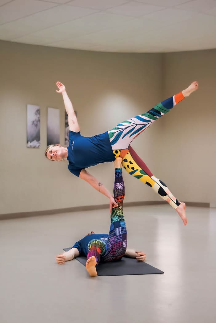 AcroYoga: Eine Frau balanciert auf dem R cken liegend miit ausgestrecktem Bein eine zweite Frau.