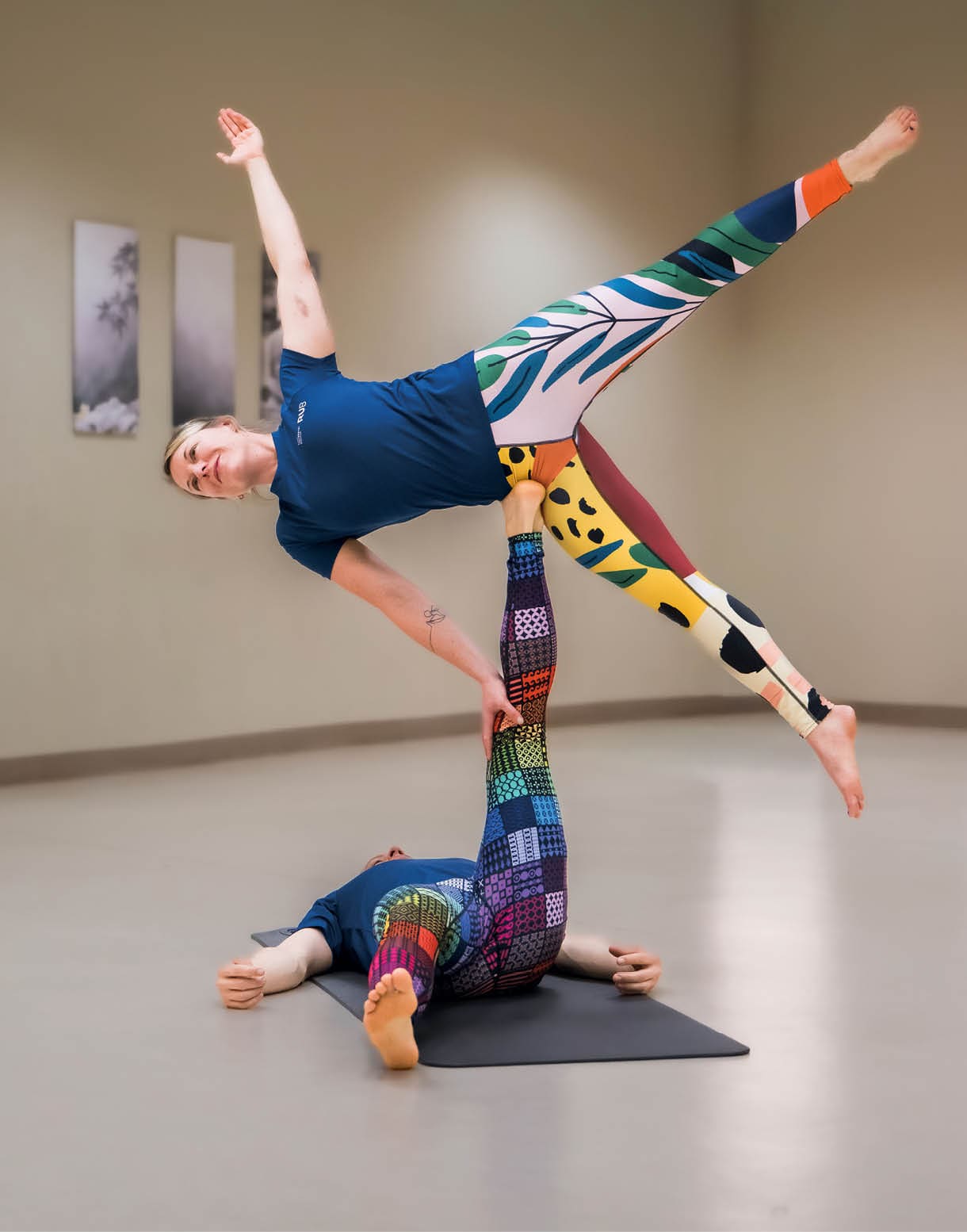 AcroYoga: Eine Frau balanciert auf dem R cken liegend miit ausgestrecktem Bein eine zweite Frau.