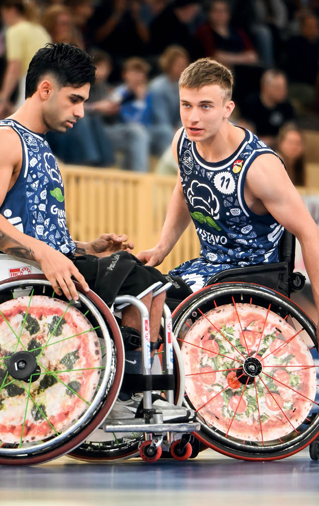 Bilder zweier Profi-Rollstuhlbasketballer w hrend eines Match. Auf den R dern der beiden Rollst hle ist eine gro e Pizza abgeblidet als Werbeanzeige f r einen Lieferservice