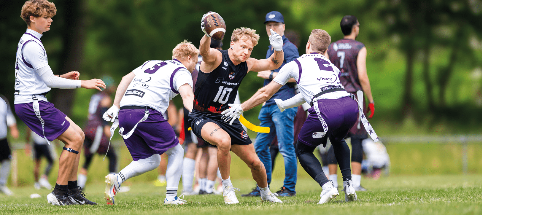 Mehrere Personen in Sportkleidung spielen auf einem Rasenfeld American Football, wobei eine Person den Ball h lt und von anderen umringt wird. Beschreibung von KI generiert