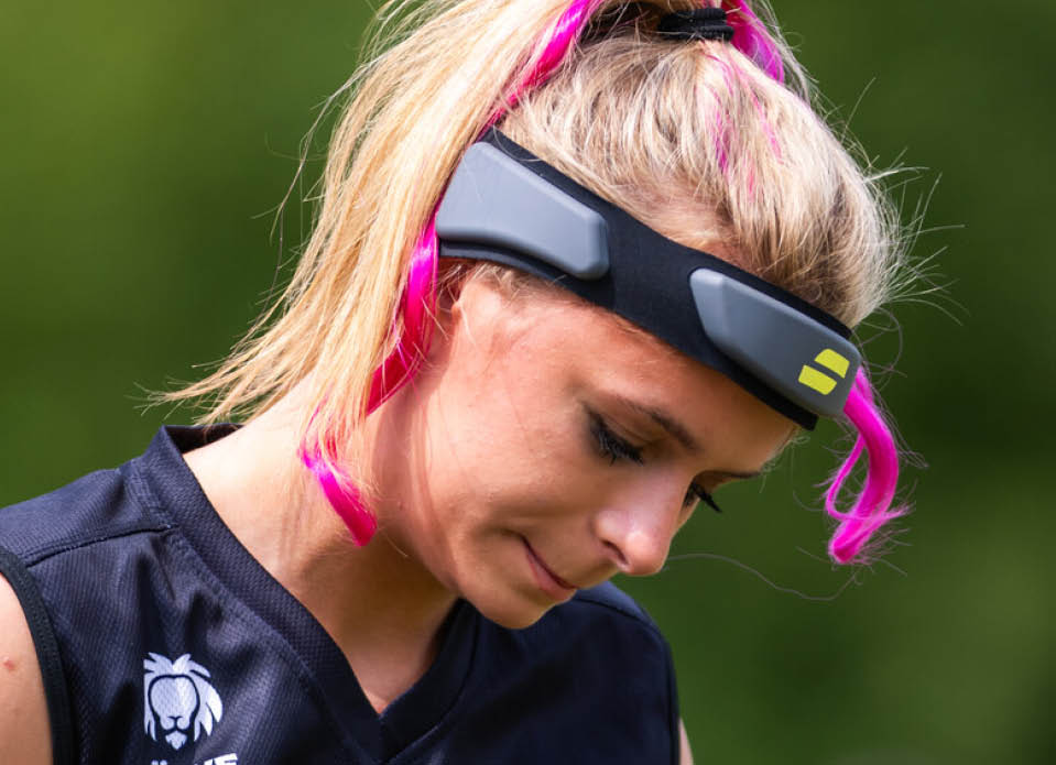 Nika Wiessner mit hellem, zum Pferdeschwanz gebundenem Haar tr gt ein schwarzes Sporttrikot und eine Sportbrille mit pinken B geln vor einem unscharfen gr nen Hintergrund. 