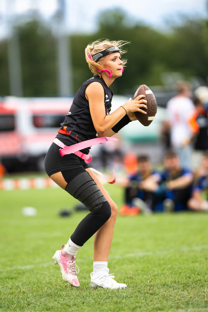 Eine Person in Sportkleidung h lt einen Football in der Hand und steht auf einem Spielfeld mit gr nem Gras. Beschreibung von KI generiert