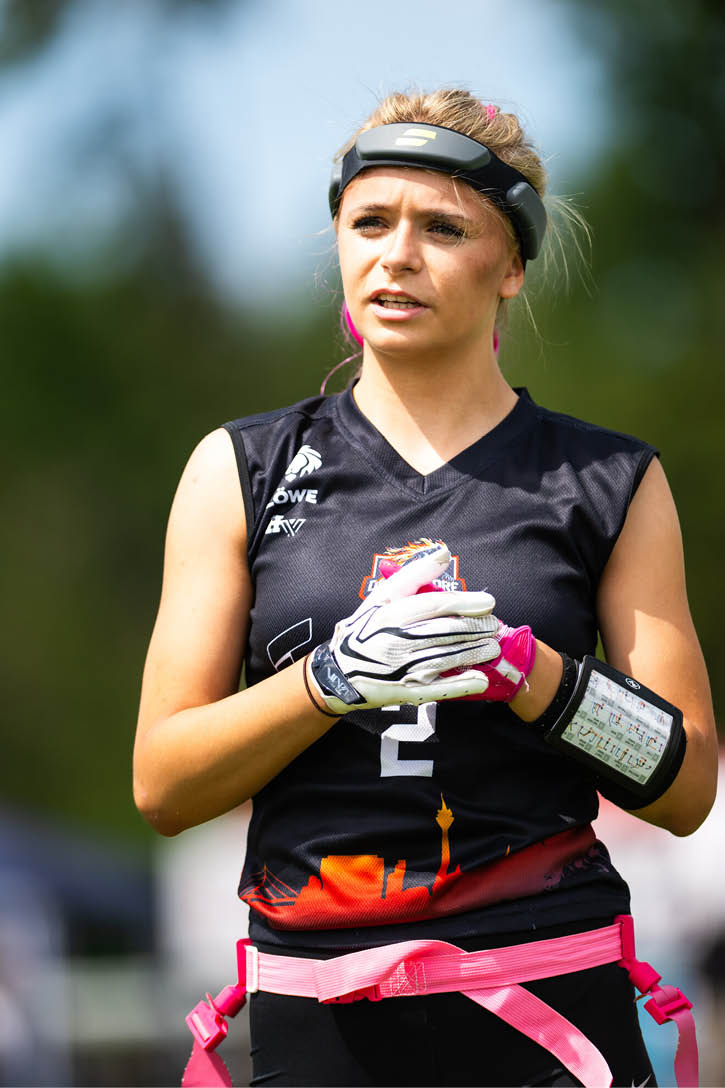 Eine Person mit Sportkleidung und Handschuhen tr gt ein Armband mit Spielz gen und steht im Freien vor unscharfem Hintergrund. Beschreibung von KI generiert