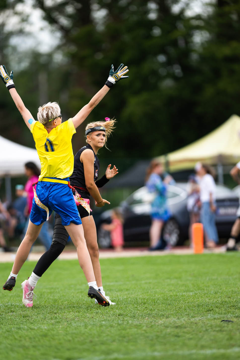 Zwei Personen in Sportkleidung spielen auf einem Spielfeld, wobei eine Person mit erhobenen Armen springt und die andere Person versucht, den Ball zu fangen. Beschreibung von KI generiert