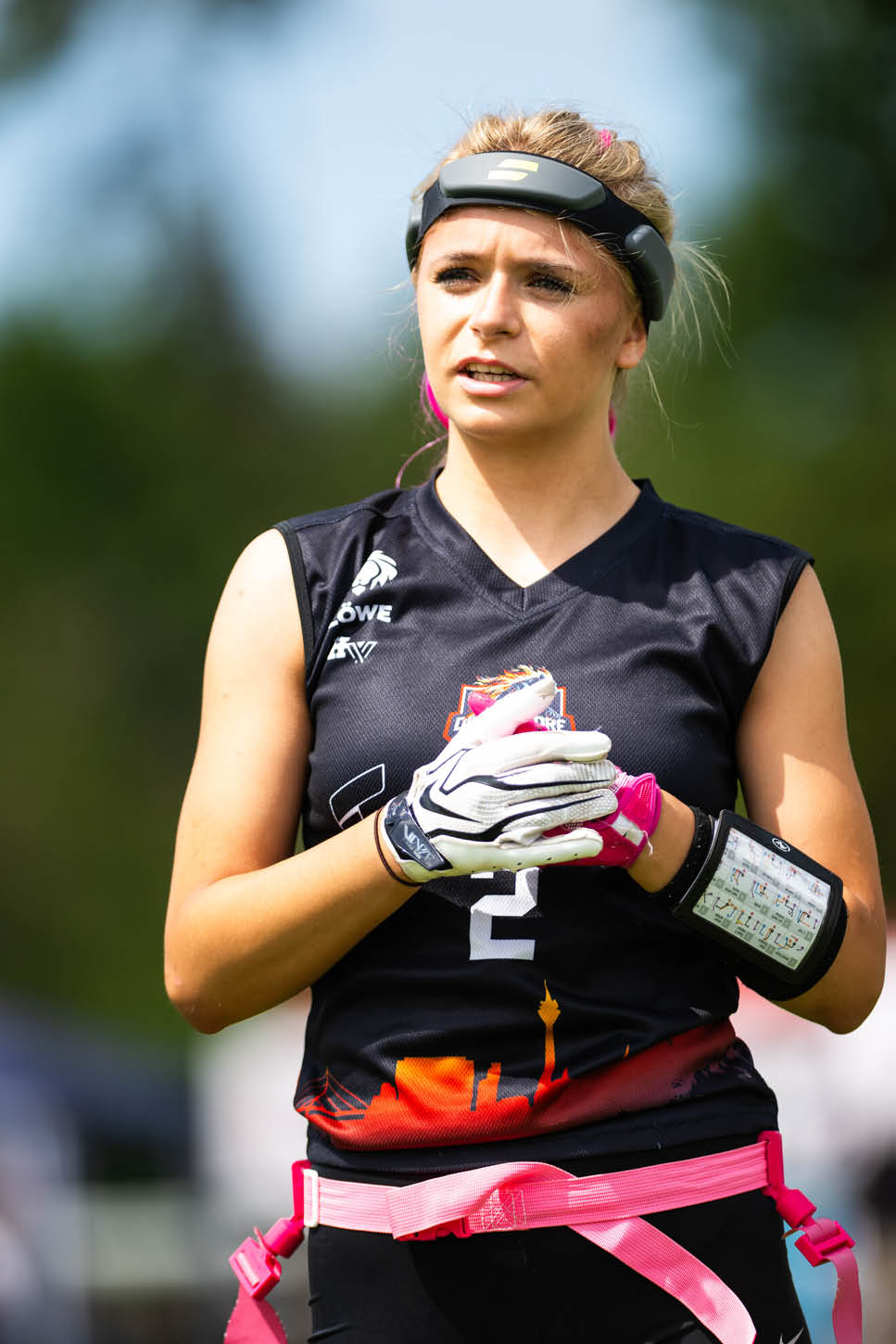 Eine Person mit Sportkleidung und Handschuhen tr gt ein Armband mit Spielz gen und steht im Freien vor unscharfem Hintergrund. Beschreibung von KI generiert