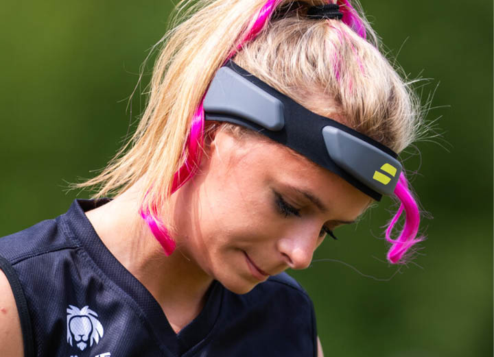 Nika Wiessner mit hellem, zum Pferdeschwanz gebundenem Haar tr gt ein schwarzes Sporttrikot und eine Sportbrille mit pinken B geln vor einem unscharfen gr nen Hintergrund. 