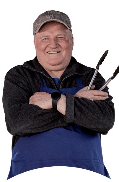 Eine Person tr gt eine blaue Sch rze und eine Kappe und h lt Grillzangen mit verschr nkten Armen.