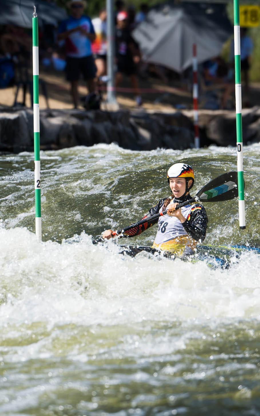 Eine Person in einem Kajak tr gt Helm und Paddel und navigiert durch wildes Wasser bei einem Kanuslalom-Wettbewerb. Beschreibung von KI generiert