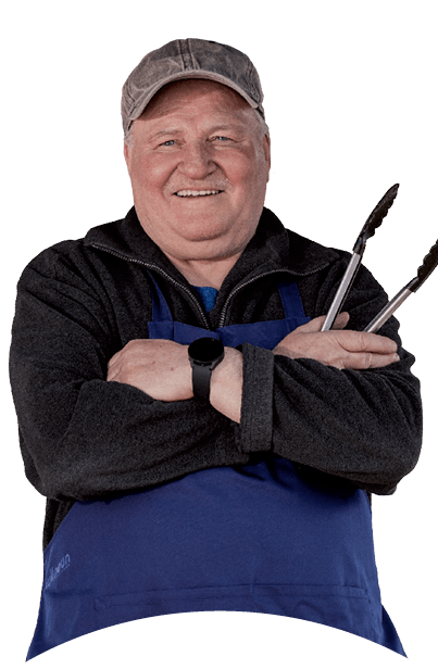 Eine Person tr gt eine blaue Sch rze und eine Kappe und h lt Grillzangen mit verschr nkten Armen.