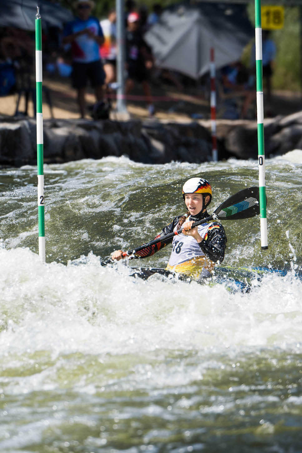 Eine Person in einem Kajak tr gt Helm und Paddel und navigiert durch wildes Wasser bei einem Kanuslalom-Wettbewerb. Beschreibung von KI generiert