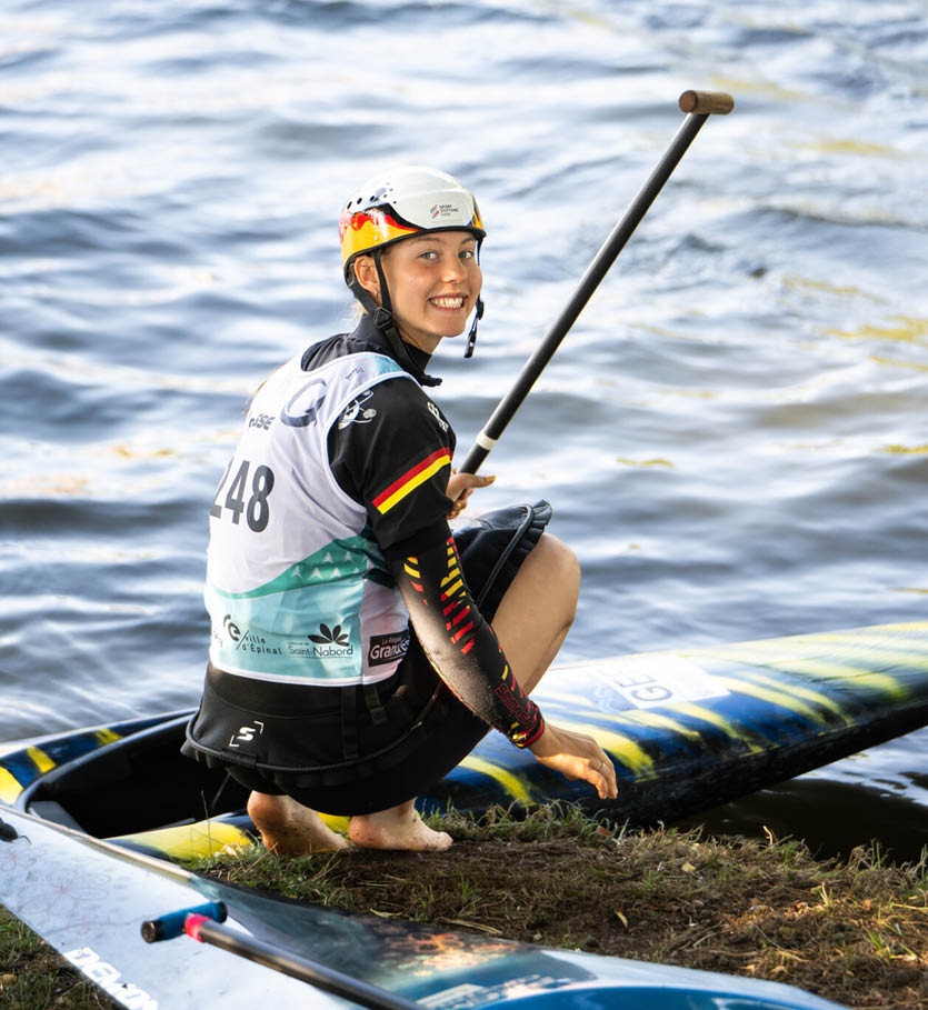 Eine Person mit Helm und Sportbekleidung sitzt auf einem Paddleboard auf einem Gew sser und h lt ein Paddel. Beschreibung von KI generiert