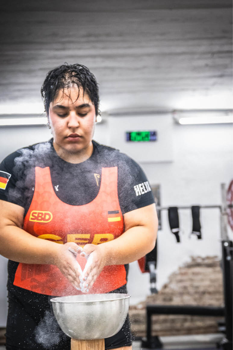 Eine Person in Sportkleidung bereitet sich in einem Fitnessstudio durch das Auftragen von Chalk auf das Gewichtheben vor. Beschreibung von KI generiert