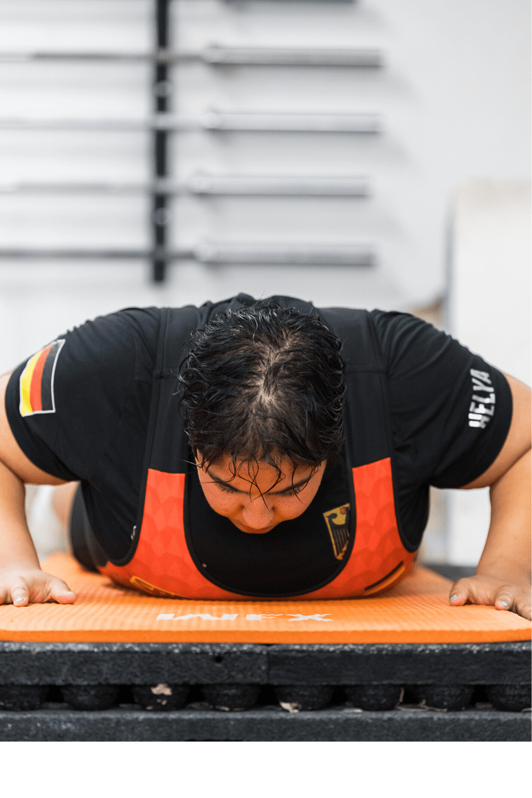 Eine Person mit schwarzem T-Shirt und rotem Trainingsanzug macht Liegest tze auf einer orangen Matte in einem Fitnessstudio. Beschreibung von KI generiert