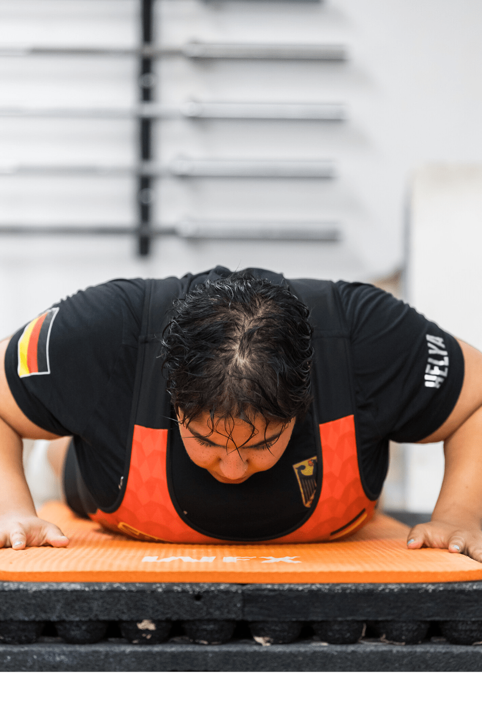 Eine Person mit schwarzem T-Shirt und rotem Trainingsanzug macht Liegest tze auf einer orangen Matte in einem Fitnessstudio. Beschreibung von KI generiert
